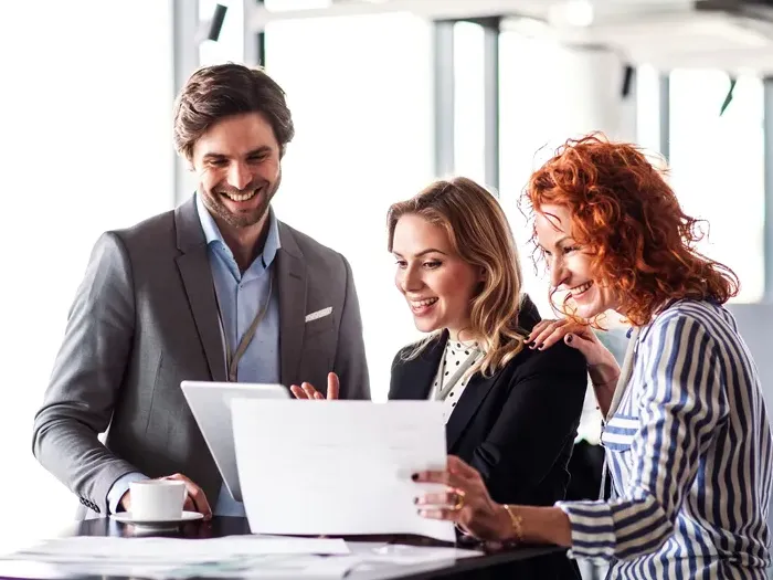 Three smiling business professionals reviewing documents and laptop during meeting in bright office for Town Service Lookup